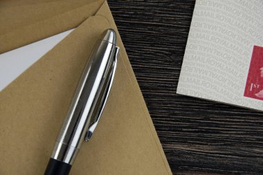 Kahverengi zarf, kalem ve pullar koyu ahşap masada.