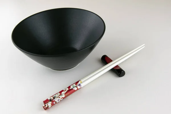 Minimalist scene of empty black bowl and chopsticks, light background