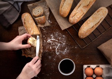 Mutfakta, ahşap kahverengi bir masanın üzerinde, yan taraftaki masa örtüsü. Yanında yumurta dolu bir karton kutu var. Sandviçler için taze ekmekler. Fırından yeni çıkmış. Eller ekmeği keser ve tereyağıyla süpürür. Bir fincan kahvenin yanında.