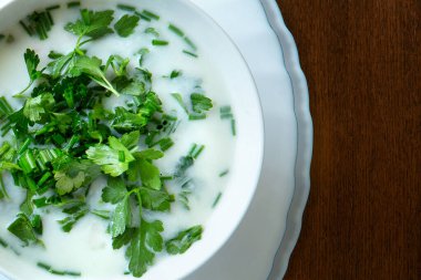 Beyaz bir tabakta maydanozlu beyaz çorba ve ahşap bir mutfak masasında yeşil soğan.