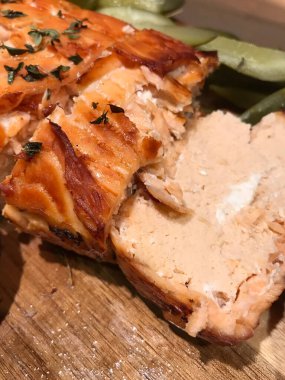 Somon filetosunun hazır pişmiş ve pembe suflesi, kekik filizleriyle süslenmiş, yanında salatalık turşusu var, masanın üzerinde ahşap bir tahtanın üzerinde.