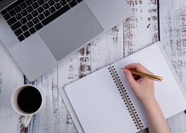 İzolasyon ya da karantina sırasında bir fincan kahveyle bilgisayardan ya da uzaktan öğrenme ve internet üzerinden çalışma. El bir deftere yazar.