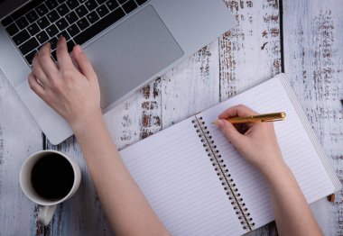 İzolasyon ya da karantina sırasında bir fincan kahveyle bilgisayardan ya da uzaktan öğrenme ve internet üzerinden çalışma. El bir deftere yazar.