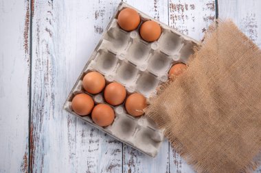 Çuval beziyle kaplı karton bir kutuda kahverengi yumurtalar, mutfakta, tahta beyaz bir masanın üzerinde yatıyor..