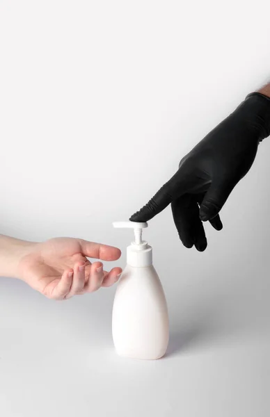 戴黑色硝酸盐手套的人把消毒剂凝胶交给另一个没有手套的人 — 图库照片