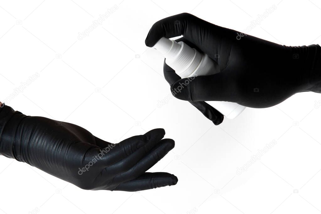 The hand of one person in a black latex glove sprays a disinfectant on the hands of another unprotected person to prevent infection during the Covid-19 epidemic and protect health.