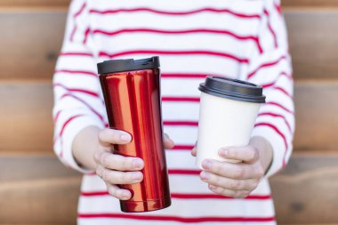 İki elinde paket kahve bardağı tutan kadın, biri plastik kapaklı tek kullanımlık kağıt bardak diğeri ise yeniden kullanılabilir paslanmaz bardak. Plastiğe hayır, saman yok, sıfır atık 