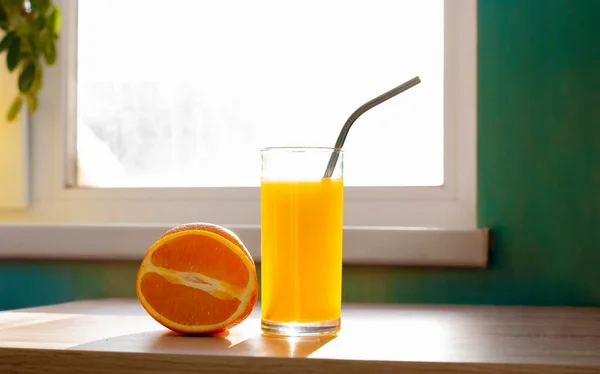 Beau fruit orange et verre de jus avec fer nont tubule en plastique près de la fenêtre sur la table image réaliste — Photo