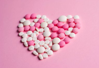 Pembe ve beyaz haplardan yapılmış güzel bir kalp sembolü. Sağlık sigortası konsepti. Pembe arkaplanda düz bir üst görünüm resmi vardı