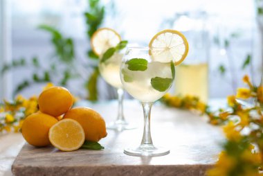 Limonlu buzlu limonata ve limon dilimi ve nane yapraklı bardaklar ve doğal arka plandaki mermer masanın üzerinde. Taze yaz içkisi güzel bir resim.