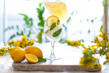 Limon dilimli buzlu sarı limonata ve nane yapraklı süsleme ve doğal arka plandaki mermer masaya dökülüyor. Taze yaz içkisi güzel bir resim. Lezzetli meyve suyu.