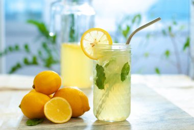 Limonlu buzlu limonata ve limon dilimi ve nane yapraklı bardaklar ve doğal arka plandaki mermer masanın üzerinde. Taze yaz içkisi güzel bir resim. Boşluğu kopyala