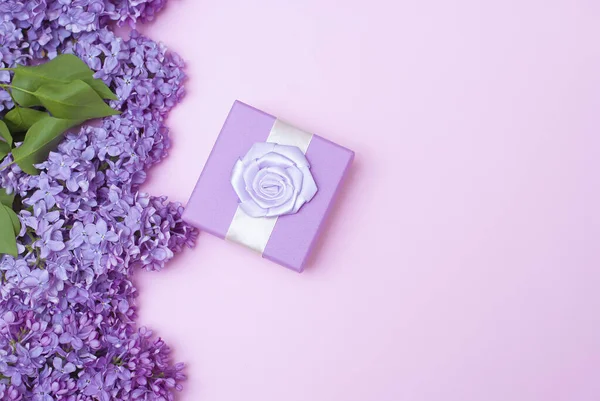 Beautiful spring lilac flowers and gift present box on light pink background. Flat lay top view picture with copy space for text. Banner top orientation. Congratulation gift card or wallpaper picture.