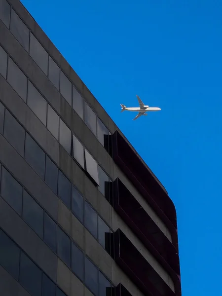 Airplane flying over office building — Stock Photo, Image