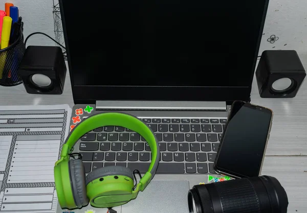 Gray laptop with headphones, cell phone and camera lens on it, with small speakers on the sides and notebook