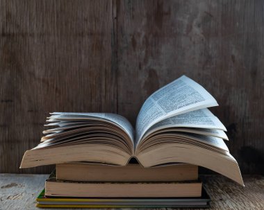 Üç kitabın üzerine açık bir kitap, ahşap bir arka plan, kitap günü kutlaması.