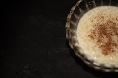 Lezzetli bir sütlü tatlı için ideal siyah zemin üzerinde pirinç pudingi ve tarçın olan cam kasenin ayrıntıları