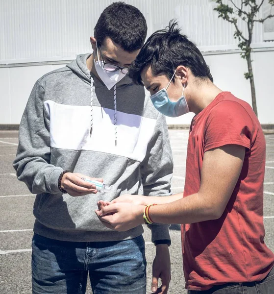 Sosyal uzaklık döneminde kendilerini covid19 'dan korumak için kendilerini dezenfekte etmek için hidroalkolik jeli paylaşan iki genç insan.
