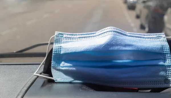 blue sanitary mask for protection against viruses placed on the dashboard of a vehicle