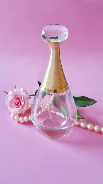 Beautiful perfume bottle, pearls and rose flower on delicate pink background