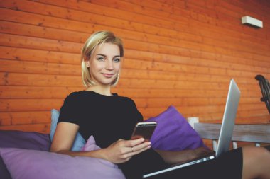 Gülümseyen genç kadın akıllı telefonla konuşma sırasında arkadaş için süre modern ortak çalışma alanı içinde oturuyor.