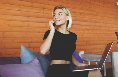 Gülümseyen genç kadın akıllı telefonla konuşma sırasında arkadaş için süre modern ortak çalışma alanı içinde oturuyor.