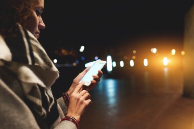 Woman tourist is searching way in navigation via cell telephone, while is standing on the street in night. 