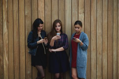 Young hipster girls dressed in trendy spring clothes are searching information on web page via their smart mobile phones