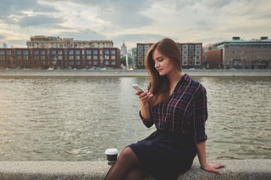 Hippi kız kısa mesaj okuma cep telefonu süre nehir Neva yakınındaki bir iskelede oturuyor.
