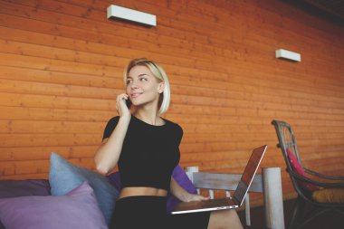 Gülümseyen genç kadın akıllı telefonla konuşma sırasında arkadaş için süre modern ortak çalışma alanı içinde oturuyor.