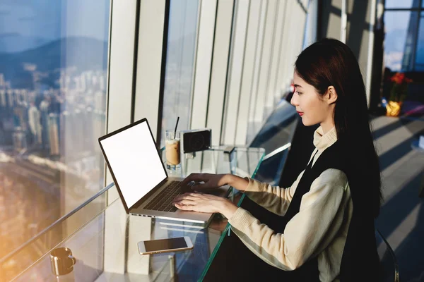 Young asian woman working with modern computer in cozy coffee shop with city space view