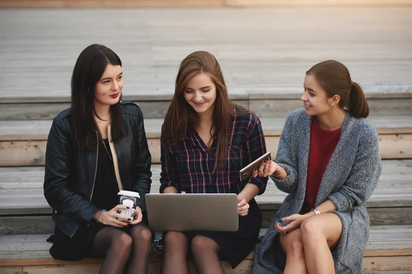 Hipster meninas com aparência moderna estão usando net-book para on-line reservar bilhetes de cinema, enquanto estão sentados ao ar livre . — Fotografia de Stock