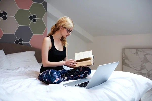 Estudiante caucásica está utilizando la literatura para el aprendizaje, mientras que se relaja con el ordenador portátil en el interior de su casa — Foto de Stock