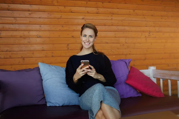 Encantadora mujer con una hermosa sonrisa está mirando a la cámara durante el chat con amigos a través de su teléfono celular — Foto de Stock