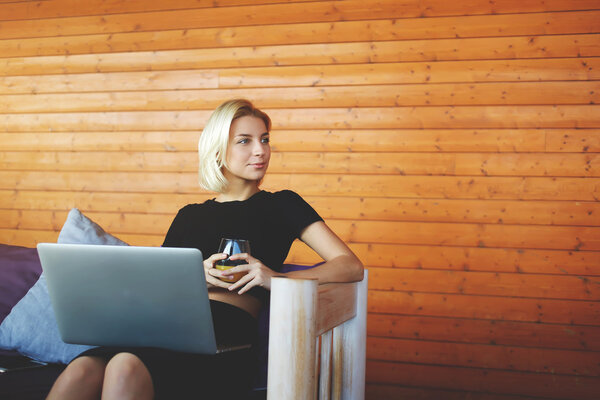 Top view of a young hipster girl is looking at the camera, while is sitting with portable net-book with empty screen in co-working space