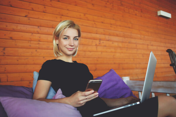 Young woman is smiling for friends during talk via smart phone, while is sitting in modern co-working space.