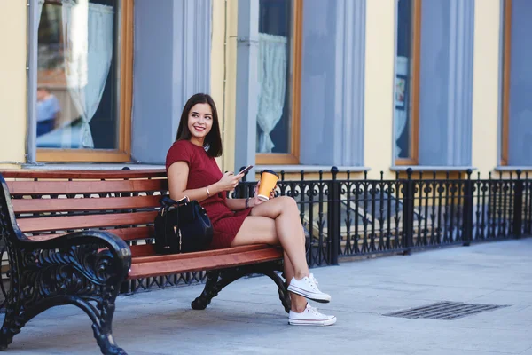 행복 한 여자는 대기 전화 그녀의 핸드폰, 동안에 밖에 서 커피와 함께 편안한 — 스톡 사진