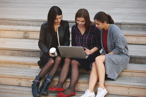 Young three hipster girls having video conversation via portable net-book, while are sitting outdoors on wi-fi zone. — ストック写真