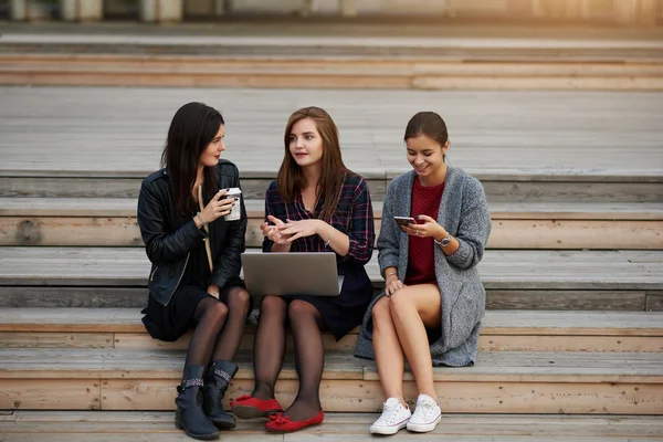 Due donne stanno parlando tra loro durante il lavoro su un net-book portatile, mentre il loro amico sta chattando su uno smartphone . — Foto Stock