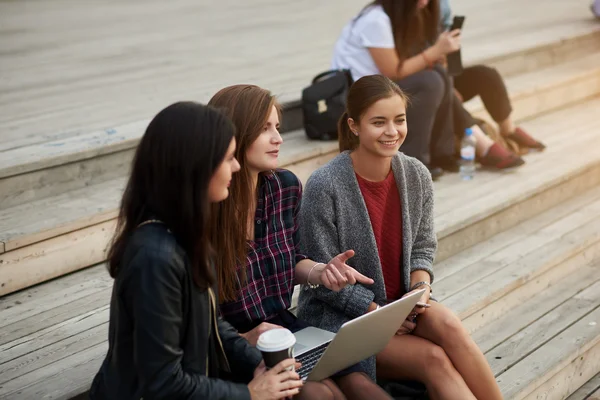 Jovens estudantes do sexo feminino ter uma conversa divertida, enquanto estão sentados com computador portátil ao ar livre no campus universitário — Fotografia de Stock