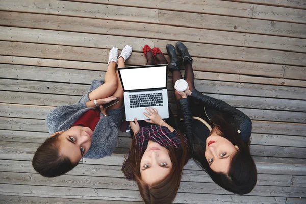 Widok z góry na trzy kobiety szukają w aparacie, siedząc z laptopem na zewnątrz na drewnianych schodach. — Zdjęcie stockowe