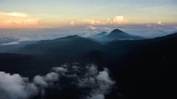 La foto aérea de la cabina del avión del cielo con las nubes blancas hinchadas con las luces de la puesta del sol sobre la silueta de las montañas por la tarde . — Foto de Stock