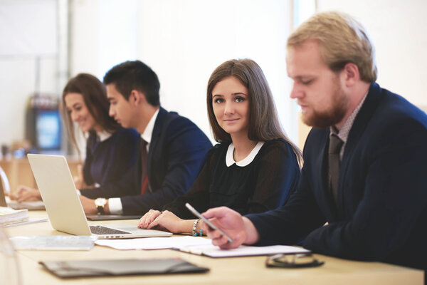 Деловая женщина позирует во время работы на ноутбуке, а ее партнер рядом чатится на мобильном телефоне
.