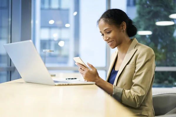 Mulher feliz via smartphone moderno conectado à rede sem fio no escritório sentado perto da área de espaço de cópia para conteúdo publicitário — Fotografia de Stock