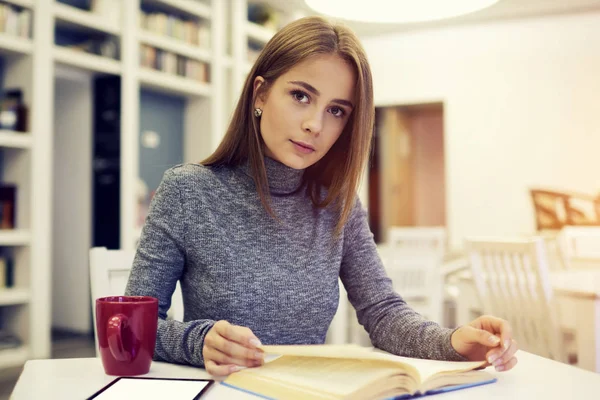 Опытная девушка сидит с чашкой чая в библиотеке — стоковое фото