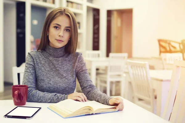 Schöne Frau sitzt am Tisch in der Universitätsbibliothek mit kostenlosem Wifi-Bereich und trinkt vor Unterrichtsbeginn heißen Kaffee zum Frühstück — Stockfoto