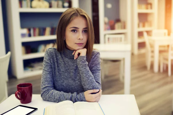 Thinking female sitting in coworking space with cup of tea and gadget connected to 5G wireless with mock up screen — Stock Photo, Image