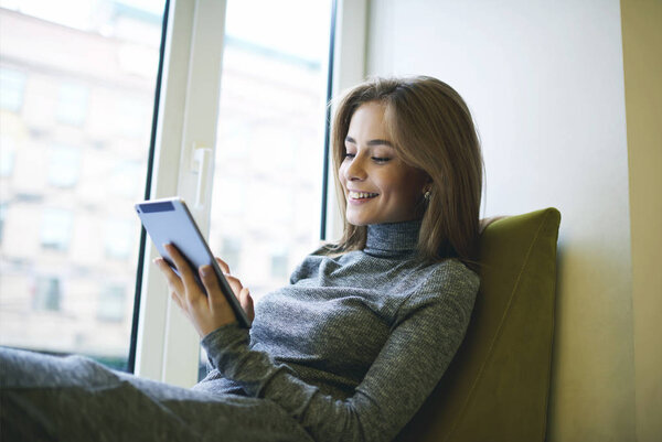 Портрет молодой привлекательной женщины расслабляющей после напряженного рабочего дня сидя у окна освещения в уютном кресле
 