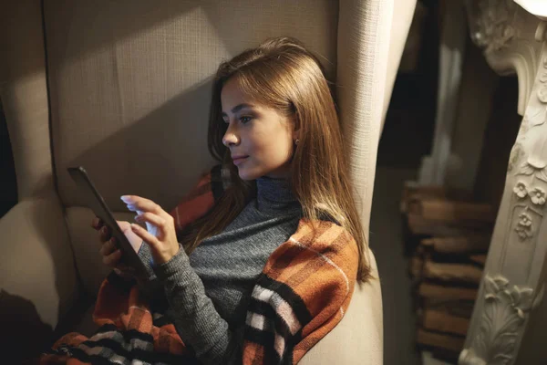 Jovem atraente feminino passar o tempo livre à noite sentado em cadeira aconchegante em casa lendo histórias favoritas — Fotografia de Stock