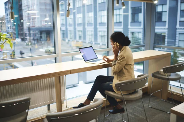 Jeune cadre afro-américain faisant un travail à distance étant en voyage d'affaires assis à table dans un espace de coworking — Photo